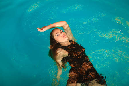 Woman relaxing at swimming pool. Young girl floating. Water aerobics fitness.の写真素材