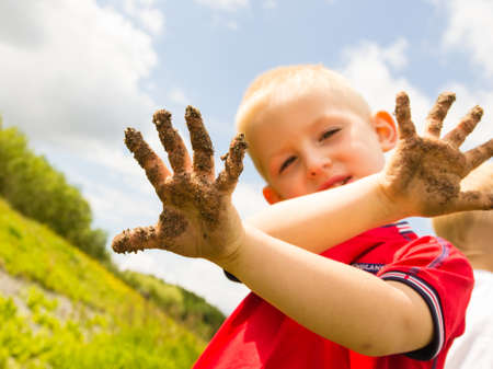 Child little blonde boy kid playing outdoor showing dirty muddy hands. Happy childhood.の写真素材