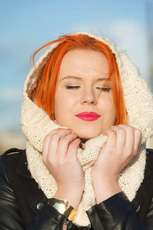 Winter fashion. Beauty face portrait red hair young woman in warm clothing white hood on head outdoor enjoying sunlight on sunny day.の写真素材