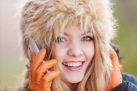 Portrait of pretty smiling fashionable woman talking on mobile phone. Happy gorgeous young girl in fur winter hat and jacket. Autumn fashion and communication.の写真素材