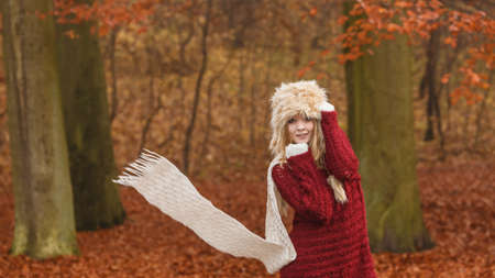 Fashion woman with flying scarf in windy fall autumn park forest against blowing wind. Young girl in fur cap having fun.の写真素材