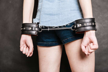 Arrest and jail. Closeup leather handcuffs on female hands, criminal woman prisoner girl back view...