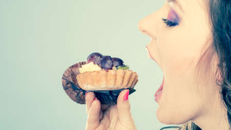 Sweet food indulging and fattening concept. Woman face profile wide open mouth eating cake cupcake filtered photoの写真素材