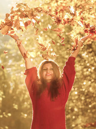 Happiness carefree. woman relaxing in autumn park throwing leaves up in the air with arms raised up. Beautiful girl in colorful forest foliage outdoor.の写真素材