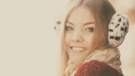 portrait of pretty smiling fashionable woman in fall forest park. happy gorgeous young girl in fur earmuffs. autumn winter fashion.の写真素材