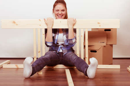 Happy woman moving in having fun assembling furniture at new home. Crazy young girl arranging...