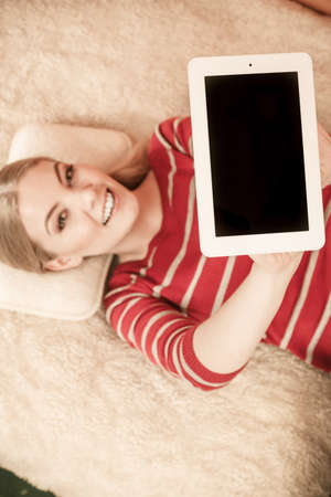 Woman laying and holding tablet computer with blank screen showing copyspace. Happy smiling woman advertising technology.の写真素材