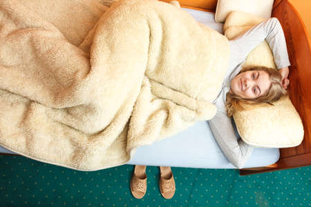 Woman waking up in bed in the morning after sleeping. Young girl laying under wool blanket.