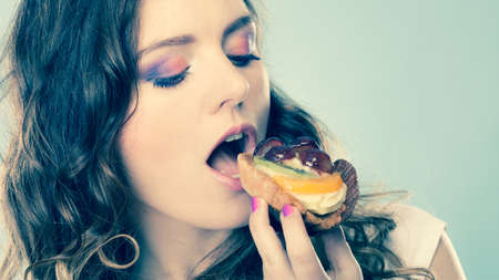 Sweet food sugar make us happy. Cute young woman colorful makeup nails holds fruit cake in hand blue...