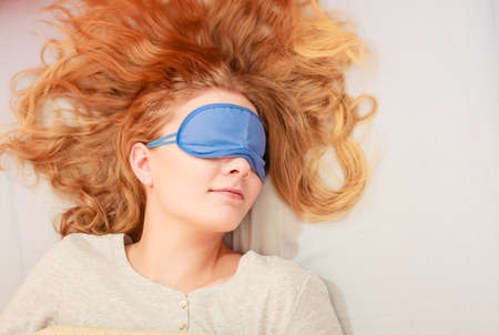 Tired woman sleeping in bed wearing blindfold sleep mask. Young girl taking nap.