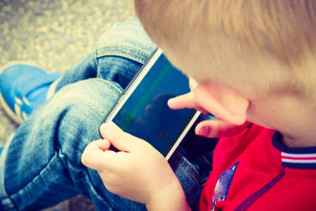 Little boy child kid playing games on smartphone mobile phone outdoor. Technology generation.の写真素材