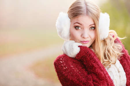Portrait of pretty attractive fashionable woman in fall forest park. Gorgeous young girl in white fur earmuffs and maroon sweater pullover. Autumn winter fashion.の写真素材