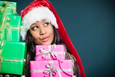 Christmas winter happiness concept. Girl mixed race woman wearing santa helper hat holding stack of...