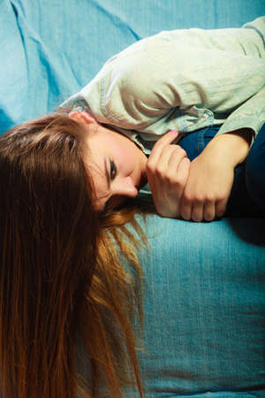 Loneliness negative emotion concept. Young sad stressed woman lying on couch at homeの写真素材
