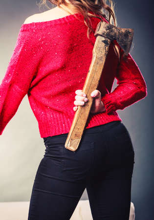 Sneaky woman holding axe. False intention. Young girl hiding chopper, axe. Back, rear view.の写真素材