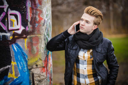 Technology and communication. Young fashion man talking on mobile cell phone using smartphone outdoorの写真素材