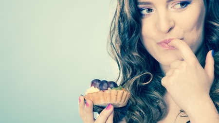 Bakery, sweet food and people concept. Closeup smiling cute woman curly hair holding fruit cake cupcake in hand on blueの写真素材
