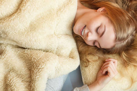 Woman waking up in bed in the morning after sleeping. Young girl laying under wool blanket.の写真素材