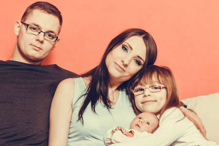 Parenthood and happiness concept. Young family mother father and child preschooler sitting on sofa with newborn baby girl at homeの写真素材