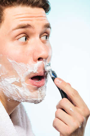 Young man shaving using razor with cream foam. Handsome guy removing face mustache hair. Skin care and hygiene.の写真素材
