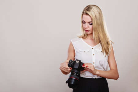 Photographer girl shooting images. Lovely blonde woman with professional camera on gray backgroundの写真素材