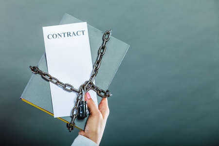 Business concept, limited by contract. Woman holding in hands paper document chained with padlockの写真素材
