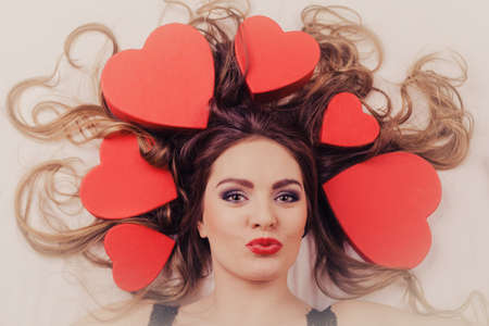 Happy woman wearing lingerie in bed at home blowing kiss. Attractive seductive young girl with heart shape boxes around head. Female underwear fashion. Valentines day love.の写真素材
