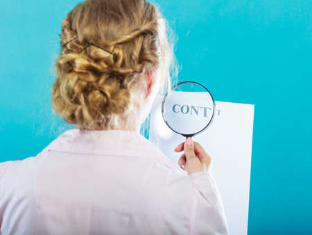 Closeup businesswoman uses magnifying glass to check contract, rear view on blue backgroundの写真素材