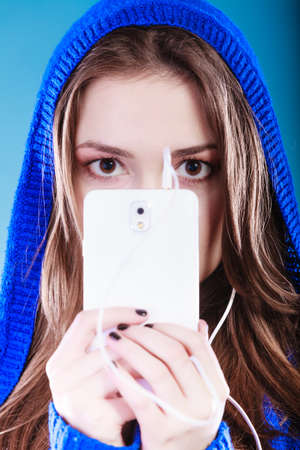 young woman with smart phone listening music. Teen stylish long hair girl in hood relaxing or...