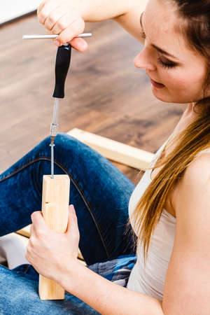 Woman assembling wooden furniture using screwdriver. DIY enthusiast. Young girl doing home improvement.の写真素材