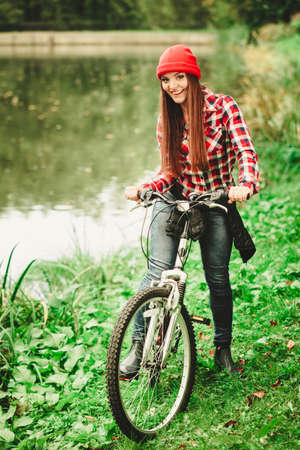 Fall active lifestyle concept. Beauty young woman sporty casual girl relaxing in autumnal park with bicycle, outdoorの写真素材