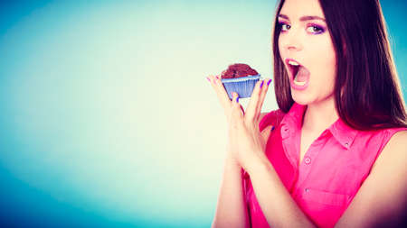 Sweet food sugar make us happy. Smiling woman holds cake chocolate muffin in hand blue backgroundの写真素材
