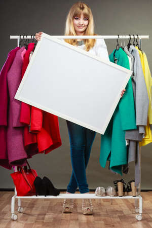 Woman in wardrobe holding blank empty banner. Girl customer in mall shop with copyspace. Fashion clothing sale advertisement.の写真素材