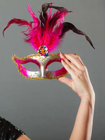Holidays, people and celebration concept. Closeup woman hand holding carnival venetian mask on gray...