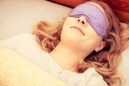 Tired woman sleeping in bed wearing blindfold sleep mask. Young girl taking nap.   の写真素材