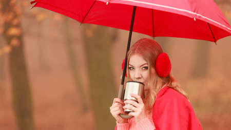 Woman with umbrella drinking hot cofee or tea relaxing in fall park. Young blonde girl resting outdoor. Autumn lifestyle fun.の写真素材