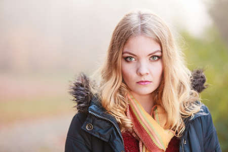 sad woman walking in fall forest park. Gorgeous blonde young girl in jacket. Autumn winter fashion. Bad emotionの写真素材