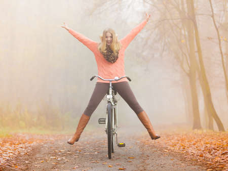 Happy carefree active woman having fun riding bike bicycle in fall autumn park. Crazy young girl in sweater relaxing. Healthy lifestyle and recreation leisure activity.の写真素材