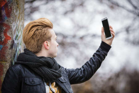 Technology internet and happiness concept. Fashionable guy taking self picture selfie with smartphone camera while walking outdoors foggy dayの写真素材