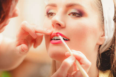 Make up artist applying lipstick with brush on pretty gorgeous woman lips. Closeup of visagiste and...