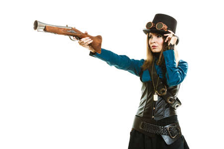Young steampunk islolated girl on white adjusting fancy hat. Fantasy old fashion with stylish topper goggle and gun aiming.の写真素材