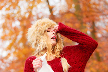 Sick ill young woman girl in fall autumn forest park sneezing into tissue.の写真素材