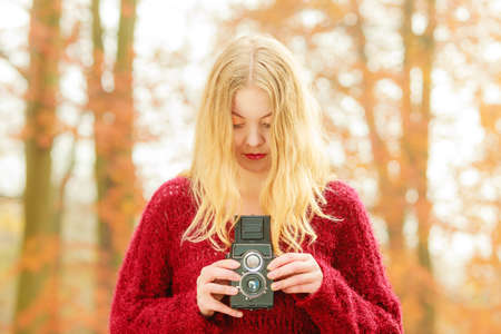 Portrait of pretty woman in fall forest park with old vintage camera. Gorgeous young girl passionate photographer. Autumn winter photography.の写真素材
