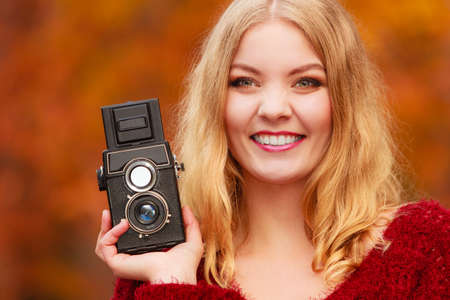 Portrait of pretty smiling woman in fall forest park with old vintage camera. Happy gorgeous young girl passionate photographer. Autumn winter photography.の写真素材