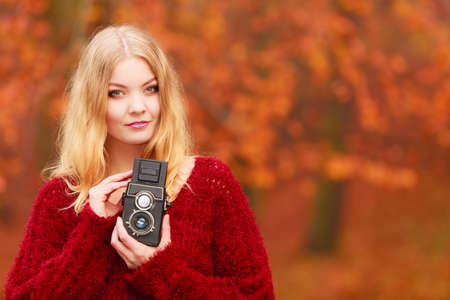Portrait of pretty smiling woman in fall forest park with old vintage camera. Happy gorgeous young...