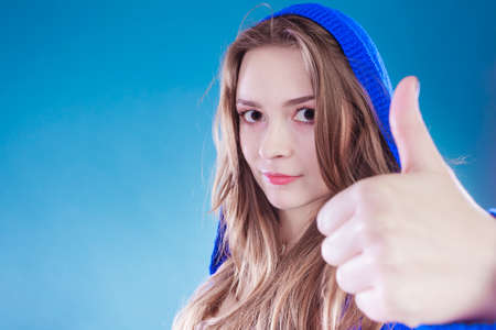Young woman giving thumbs up sign. Pretty girl in sweater with hood on head.の写真素材