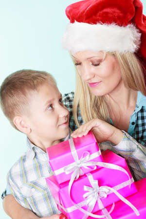 Happy childhood, holidays christmas time. Mother in santa claus hat and little boy child with stack of pink presents gift boxes on blueの写真素材