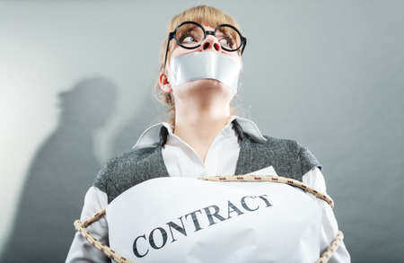 Afraid businesswoman bound by contract terms and conditions with mouth taped shut. Scared woman tied to chair become slave. Business and law concept.の写真素材