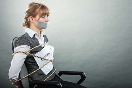 Afraid businesswoman bound by contract terms and conditions with mouth taped shut. Scared woman tied to chair become slave. Business and law concept.の写真素材