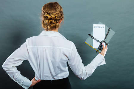Business concept, limited by contract. Woman holding in hands paper document chained with padlockの写真素材